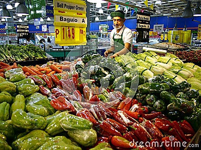 A worker arranges fresh fruits and vegetables on a shelf at a grocery store in Antipolo City. Editorial Stock Photo