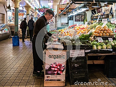 Worker arranges organic produce at Pike Place Public Market, Sea Editorial Stock Photo