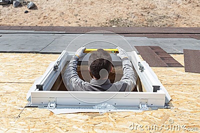 Worker on a asphalt shingle roof installing new plastic mansard or skylight window. Editorial Stock Photo