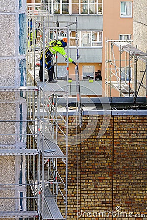 The worker assembles the scaffolding on the facade of a multi-storey house at a dangerous height Editorial Stock Photo
