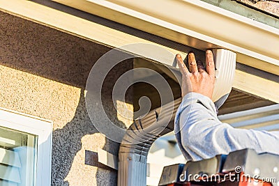 Worker Attaching Aluminum Rain Gutter and Down Spout to Fascia of House Stock Photo
