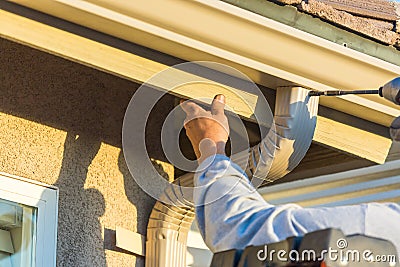 Worker Attaching Aluminum Rain Gutter and Down Spout to Fascia o Stock Photo