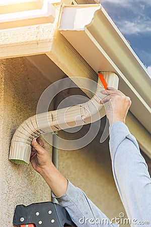 Worker Attaching Aluminum Rain Gutter and Down Spout to Fascia o Stock Photo