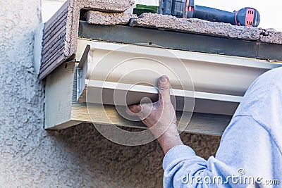 Worker Attaching Aluminum Rain Gutter to Fascia of House Stock Photo