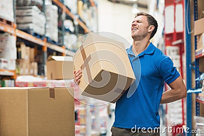 Worker with backache while lifting box in warehouse Stock Photo