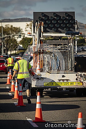 Worker behind utility truck placing bright orange traffic cones on roadway f Editorial Stock Photo