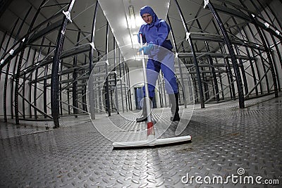 Worker in blue, protective coveralls cleaning floor in empty storehouse Stock Photo