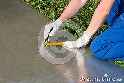 worker in blue uniform and gloves, marks the line of cutting off the yellow ruler sheet of polycarbonate Stock Photo