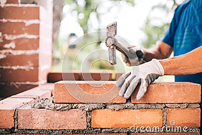 Worker building exterior walls, using hammer for laying bricks in cement. Detail of worker with tools Stock Photo