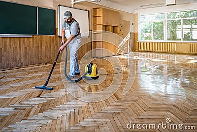 Worker carpenter cleans the parquet floor with professional vacuum cleaner. Industrial theme Stock Photo