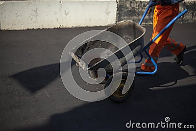 The worker carries the cart. Road repair. The loader is dragging the broken asphalt in a one-wheeled cart. Stock Photo