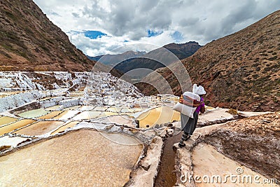 Worker carrying a big sack of salt, on the terraced salt pans in Maras, Urubamba Valley, Peru. Manual work in developing countries Editorial Stock Photo