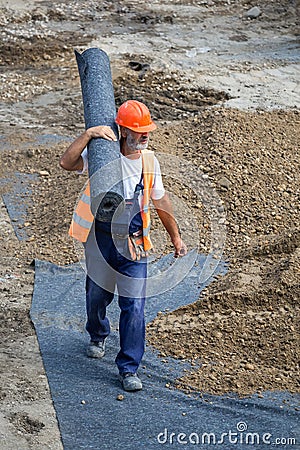 Worker carrying rolls of geotextile insulation Editorial Stock Photo