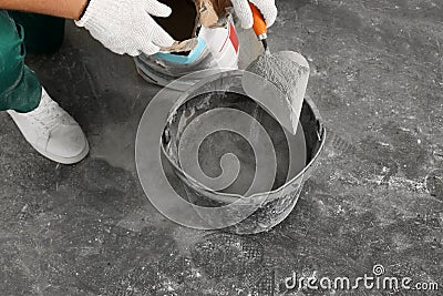 Worker with cement powder and trowel mixing concrete in bucket indoors, closeup Stock Photo