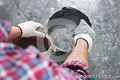 Worker with cement powder and trowel mixing concrete in bucket indoors, closeup Stock Photo