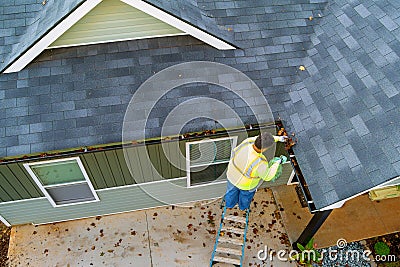 A worker is cleaning clogs in roof gutter drain by picking up dirt, debris, fallen leaves Stock Photo