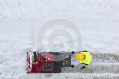 Worker cleaning snow on the sidewalk with a snowblower. Wintertime Editorial Stock Photo