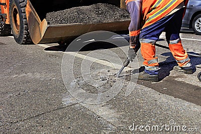 A worker clears a piece of asphalt with a pneumatic jackhammer in road construction Stock Photo