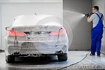 Worker covering automobile with foam at car wash. Stock Photo