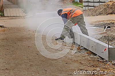 A worker cuts a curb with a circular saw at a construction site. Editorial Stock Photo