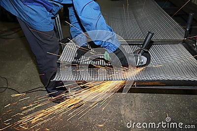 A worker cuts an iron mesh netting with an iron circle. Sparks fly Stock Photo