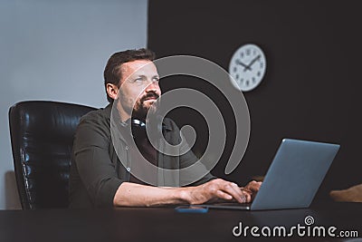 Worker daydreaming while sitting in office. Man dressed in casual wear, typing on laptop. However, distant gaze and Stock Photo