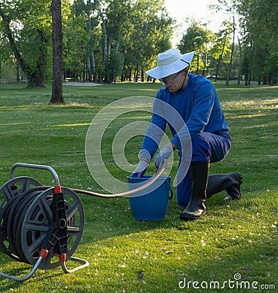 A worker fills water into a bucket,maintaining the greenery image Stock Photo