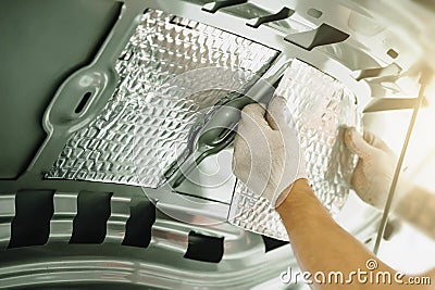 Worker glues soundproofing material to inside of car hood. Process of car sound insulation installation Stock Photo