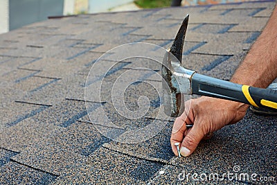 Worker hands installing bitumen roof shingles. Worker Hammer in Nails on the Roof. Roofer is hammering a Nail in the Roof Shingles Stock Photo