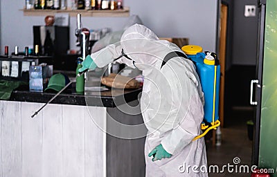 Worker in hazmat suit wearing face mask protection while making disinfection inside bar restaurant - Coronavirus decontamination Stock Photo