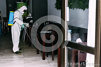 Worker in hazmat suit wearing face mask protection while making disinfection inside bar restaurant - Coronavirus decontamination Stock Photo