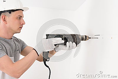A worker in a helmet makes a hole in a concrete wall with a puncher Stock Photo