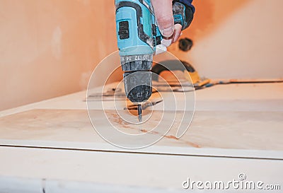 Worker is holding in hands electric drill and cutting panels in apartment. Maintenance repair works renovation in the flat with Stock Photo