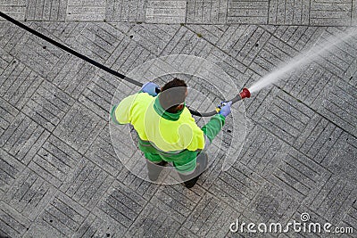 Worker holding a hose cleaning the sidewalk with water Editorial Stock Photo
