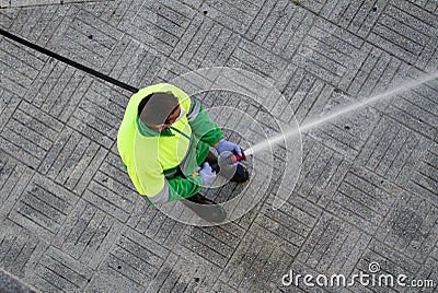 Worker holding a hose cleaning the sidewalk with water Editorial Stock Photo