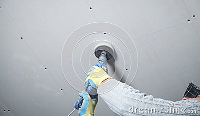 Worker holding a power drill. Make a hole in the ceiling. Install lamp Stock Photo