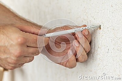 Worker inserts plastic wall plug into a hole. Stock Photo