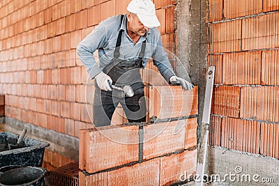 Male worker installing bricks with mortar and rubber hammer. Construction industry details Stock Photo