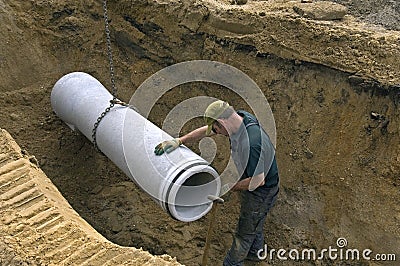 Worker laying new sewer pipe in slot in the street Editorial Stock Photo