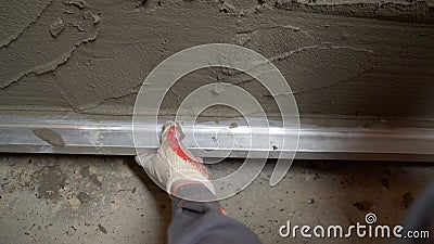 Builder using shape rule for plastering brick wall. The worker levels the wall using a rule Stock Photo