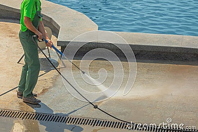 Worker man in uniform washes street or park sidewalk near water pool or fountain. Municipal service of city cleaning process. Guy Stock Photo