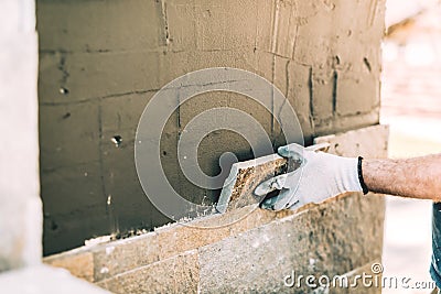 Worker mason closely placing stone tile on vertical wall. Industry details - construction site Stock Photo