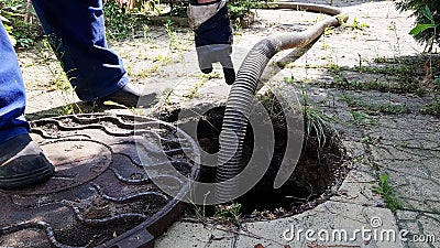 the worker opened the sewer hatch and inserted a hose for cleaning the septic tank. maintenance of communications in a Stock Photo