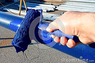 Worker paints steel pipe with roller to prevent rust. Blue paint Stock Photo