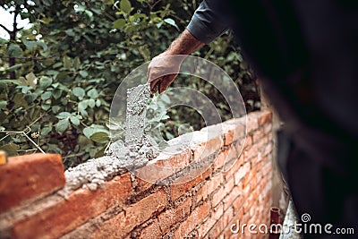 Worker placing and installing bricks on exterior wall on house construction. Worker using mortar, trowel and putty knife Stock Photo