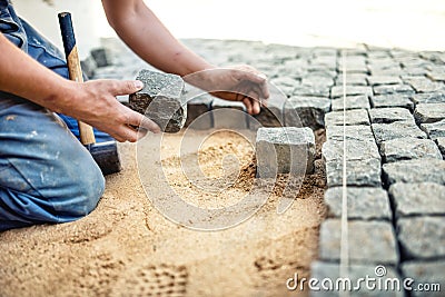 Worker placing stone tiles in sand for pavement, terrace. Worker placing granite cobblestone pavement at local terrace Stock Photo