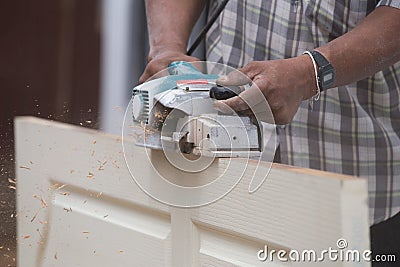 Worker planing a wood of door with electric plane Stock Photo