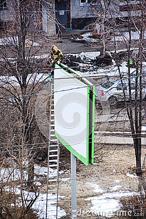 Worker prepares billboard to installing new advertisement. Industrial climber working on a ladder - placing Stock Photo