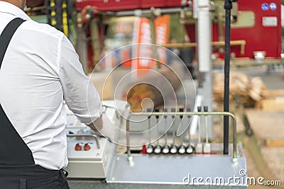 Worker pressing buttons on CNC machine control board in factory. Partially milled log on a portable lumber milling machine. Stock Photo
