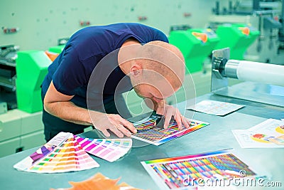 Worker in a printing and press center uses a magnifying glass to check the print quality. Scene showing the print quality control. Stock Photo